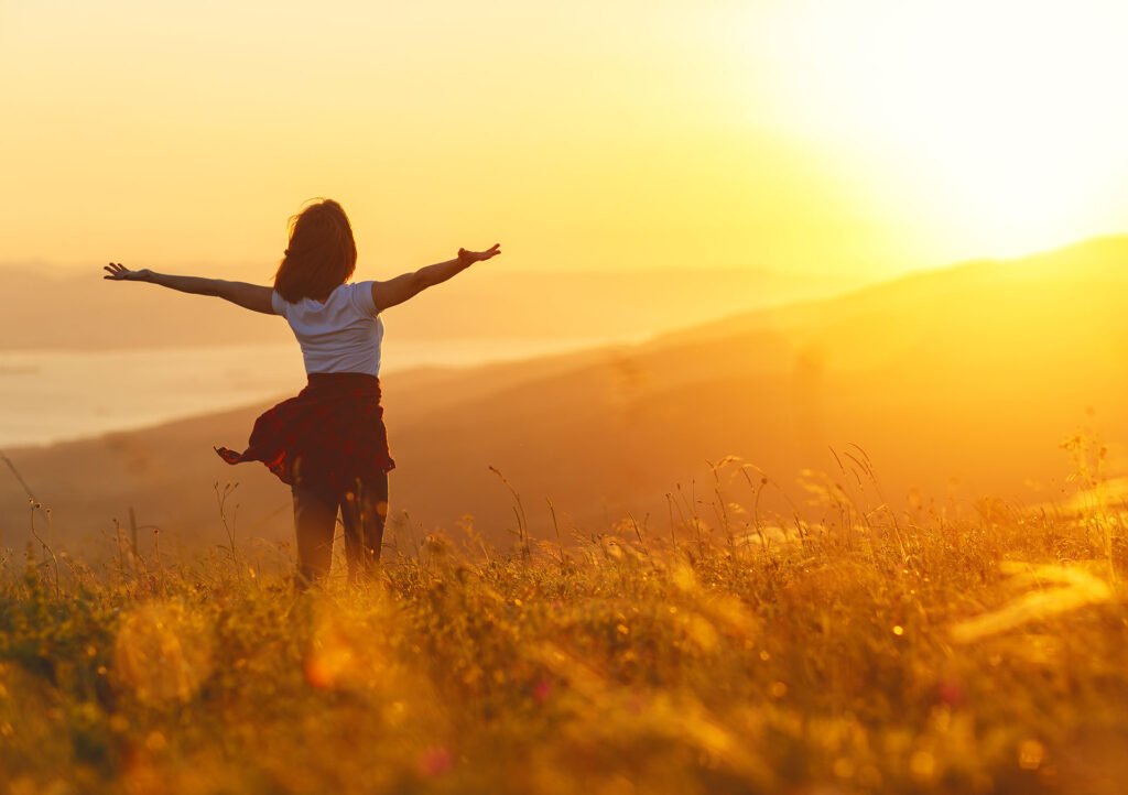woman cheering in field at sunrise